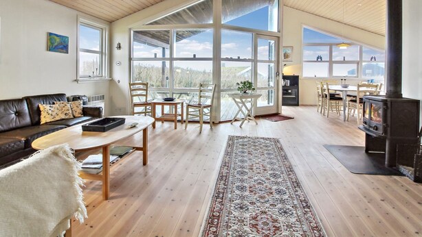 Amplia sala de estar con techo alto, piso de madera, chimenea y ventanas grandes que ofrecen vistas al exterior.
