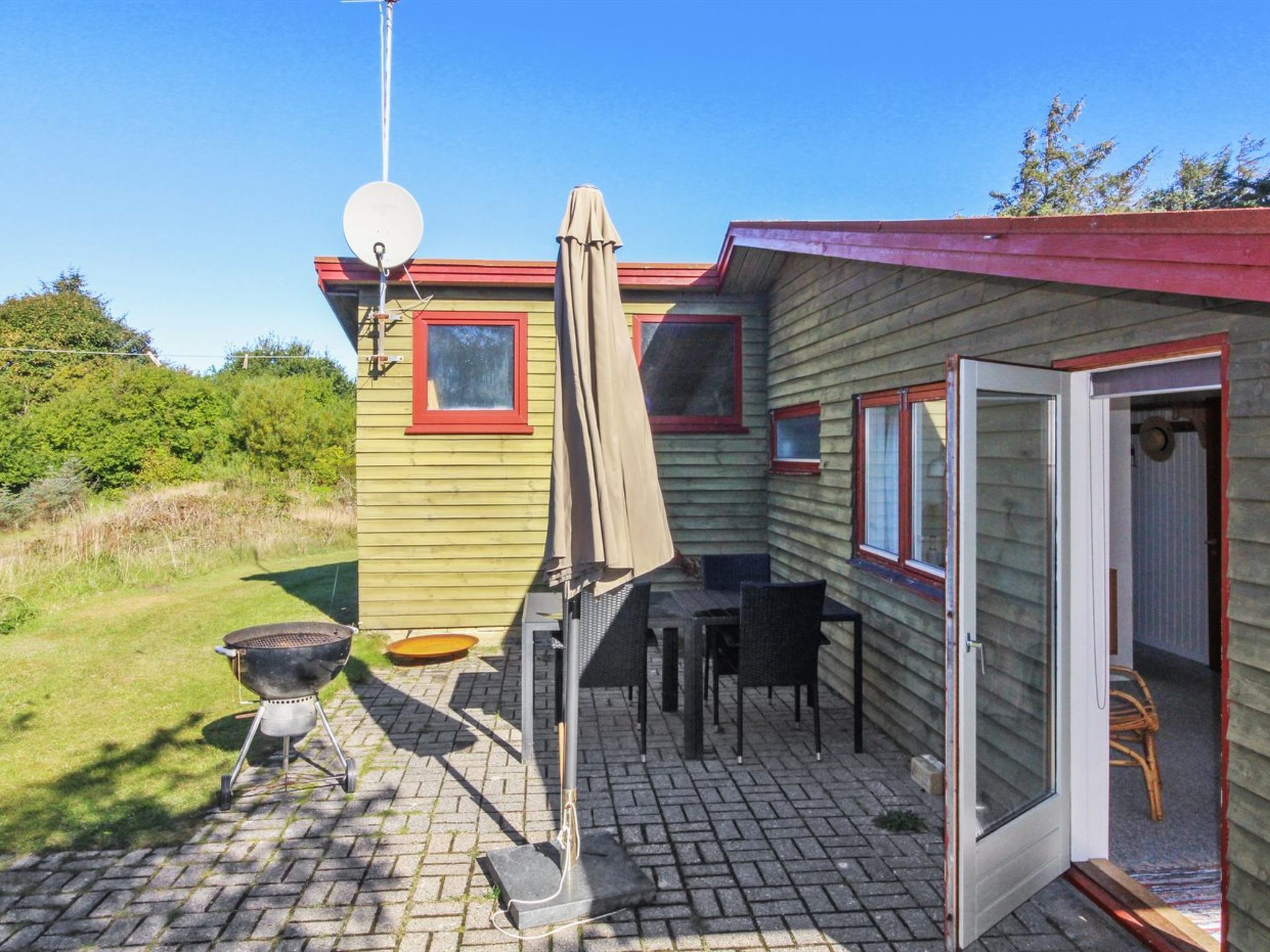 Une petite maison de plain-pied dotée d’un patio comprenant un barbecue, du mobilier d’extérieur et une antenne parabolique.