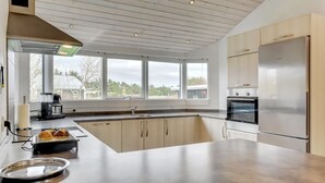 A modern kitchen with a large island, stainless steel appliances, and large windows offering a view of the outdoors.