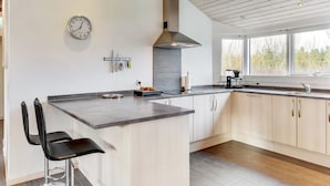 A modern kitchen with a central island, wooden cabinets, a stainless steel sink, and a large window providing natural light.