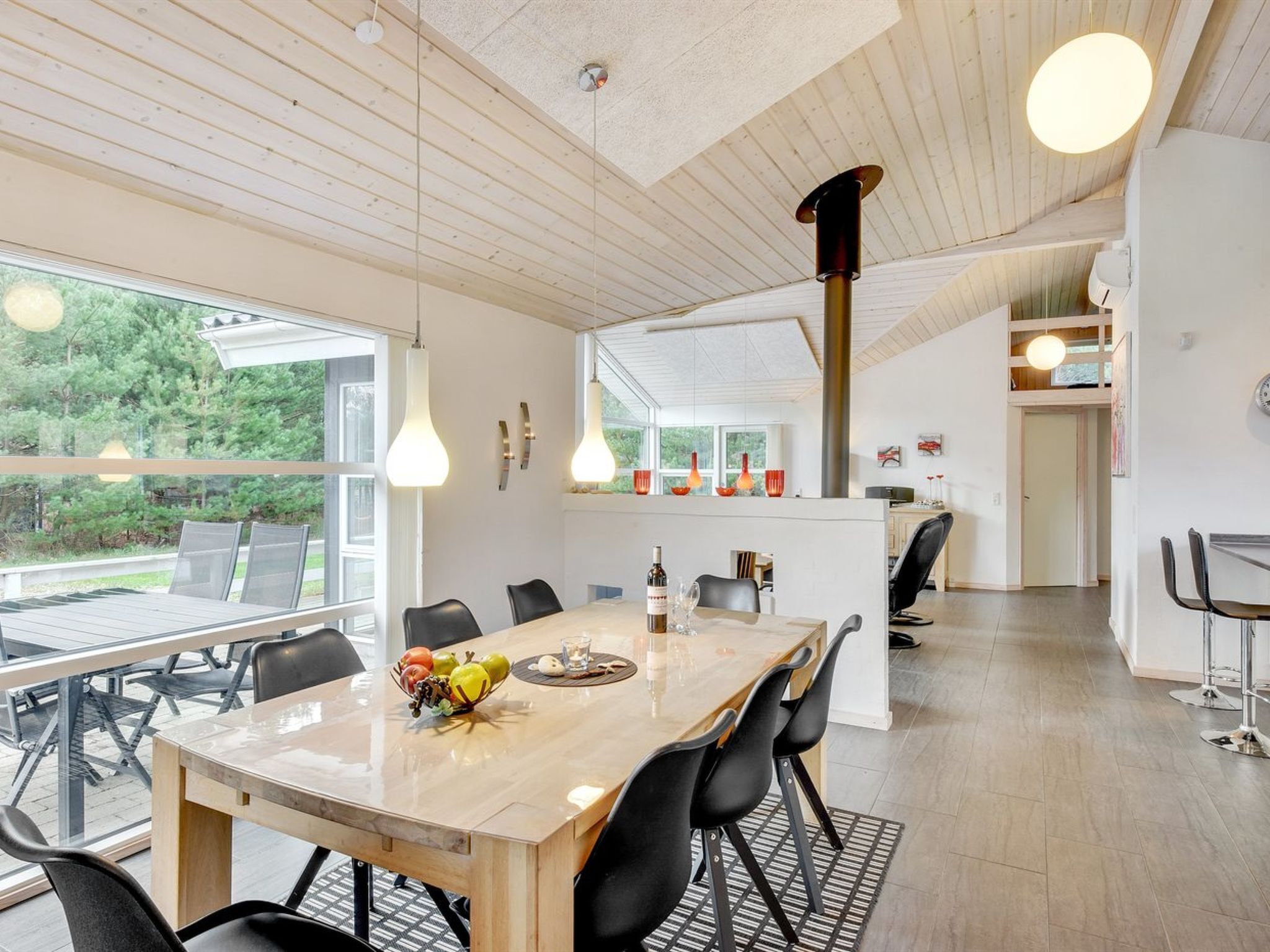 Una cocina moderna con una mesa y sillas de madera, un frutero y lámparas colgantes.