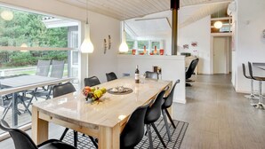 A modern kitchen with a wooden table and chairs, a fruit bowl, and hanging pendant lights.