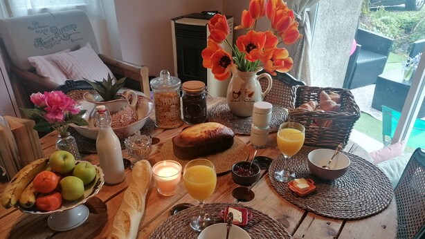 A breakfast table with bread, fruits, a candle, and a vase of flowers. - Suite Noelie, son Ecran de Cinema et sa Baignoire d Époque (Brassac)