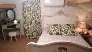 A bedroom with a bed, a vanity with a mirror, a stool, a nightstand with a lamp, and an air conditioning unit. - Suite Noelie, son Ecran de Cinema et sa Baignoire d Époque (Brassac)