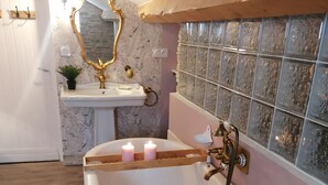 A bathroom with a freestanding bathtub filled with water and rose petals, a vanity with a mirror, and a decorative wall with a tiled backsplash. - Suite Noelie, son Ecran de Cinema et sa Baignoire d Époque (Brassac)