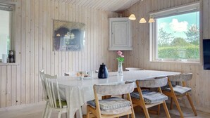 En matplats med ett runt bord, stolar, en vas med blommor och ett fönster med utsikt över grönområden.