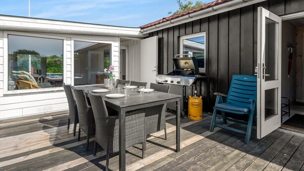 En täckt uteplats med ett matbord, stolar, en grill och en gasolflaska.