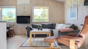 Ett mysigt vardagsrum med ett träpanelat tak, en grå soffa, en brun läderfåtölj, ett träbord och en tv som är monterad på väggen.