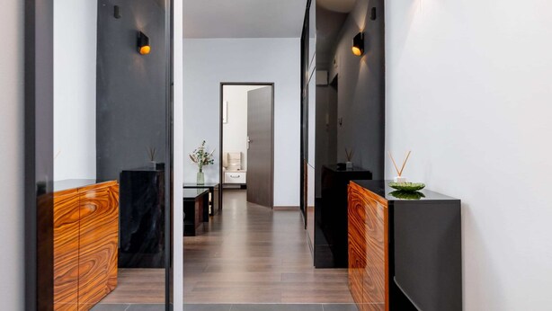 Un couloir moderne avec un banc en bois, une console noire et une cloison en verre.
