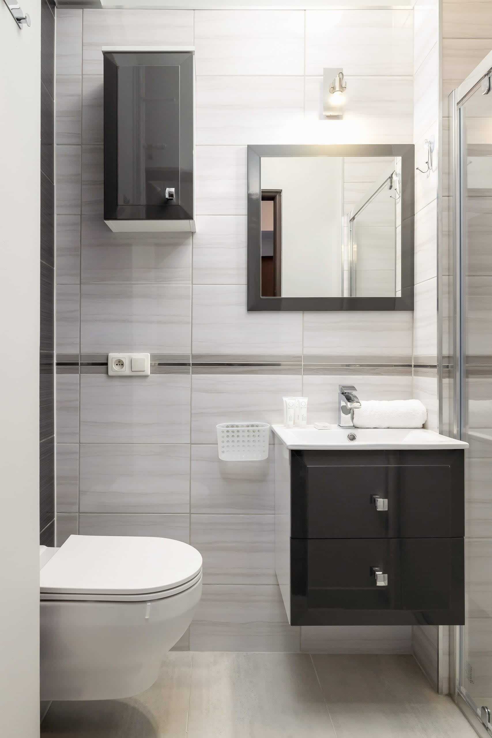 Een moderne badkamer met toilet, wastafel met spiegel erboven en een douchehoek.