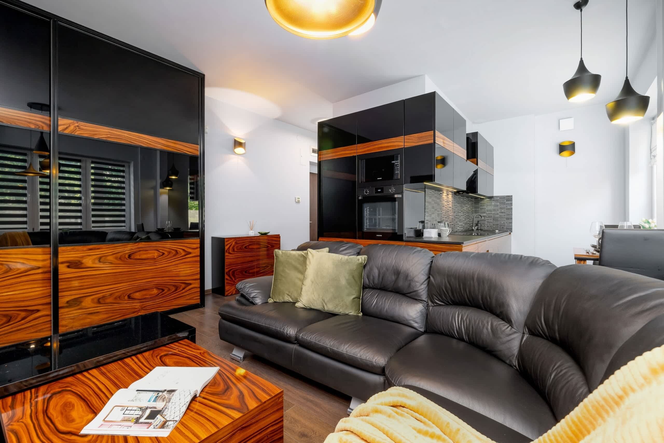 A modern living room with a leather sofa, wooden furniture, and a kitchen area with black cabinets and a built-in oven.