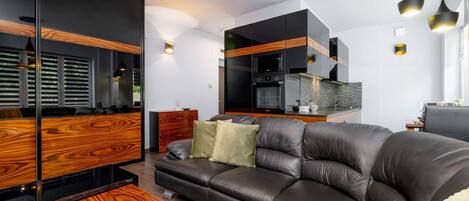 A modern living room with a leather sofa, wooden furniture, and a kitchen area with black cabinets and a built-in oven.
