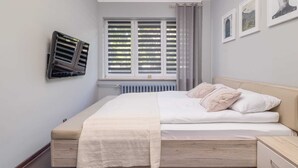 Une chambre à coucher comprenant un lit, des tables de chevet, un radiateur, une fenêtre avec des stores et un climatiseur fixé au mur.