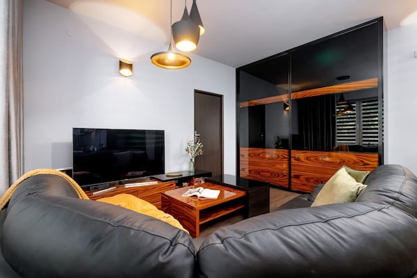Una sala de estar moderna con televisor de pantalla plana, sofá de cuero, mesa de centro de madera y un espejo grande.