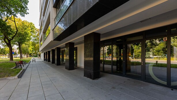 Un edificio moderno con una galería techada, grandes ventanales y terraza al aire libre.