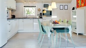 Uma cozinha moderna com armários brancos, uma mesa de jantar com cadeiras verde-água e uma tigela de frutas.