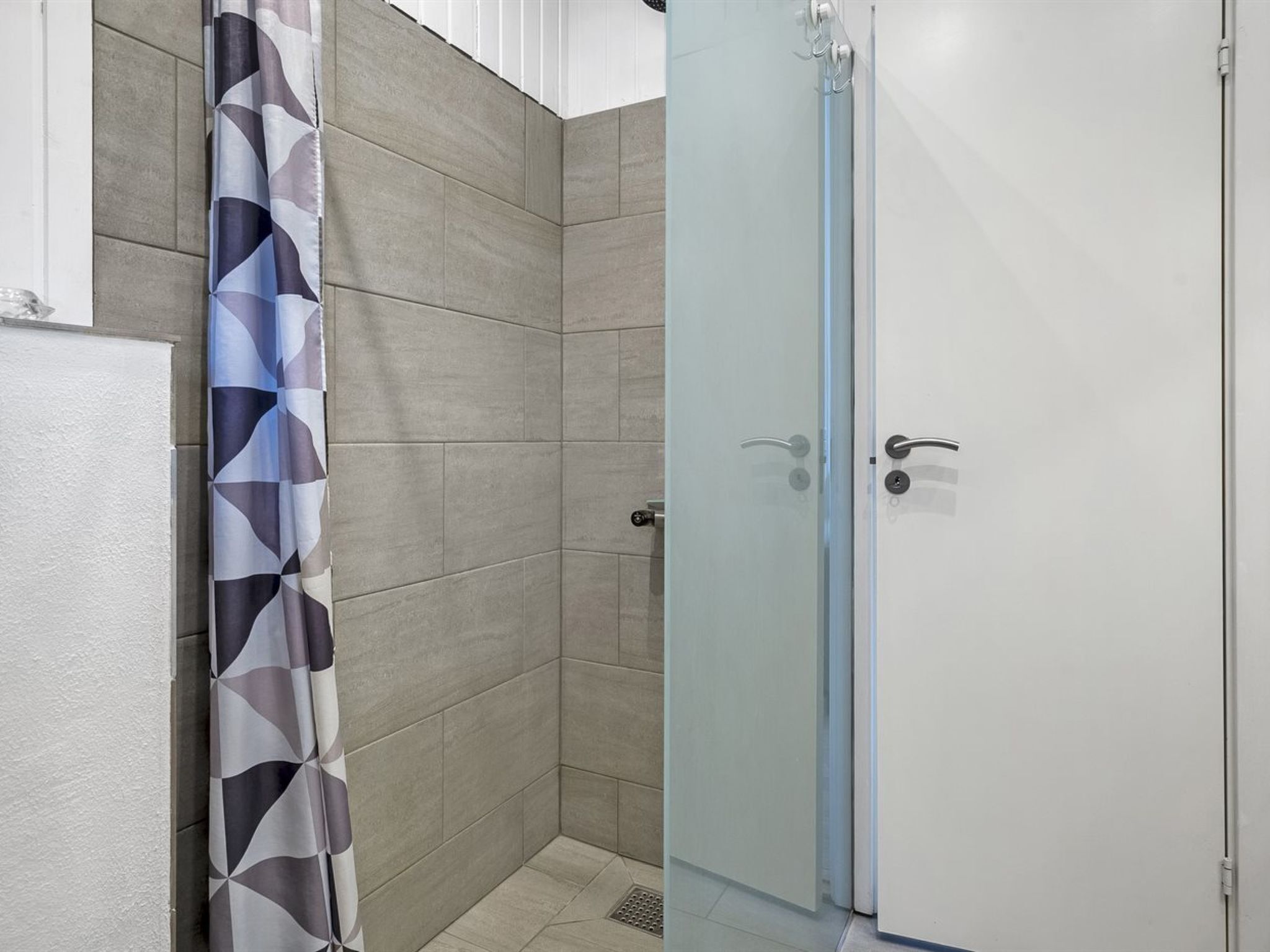 Un angolo doccia con porta in vetro, pareti piastrellate e tenda decorata.