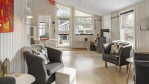 Uma sala de estar ampla com lareira, sofá, mesa de jantar e uma grande janela com vista para o exterior.