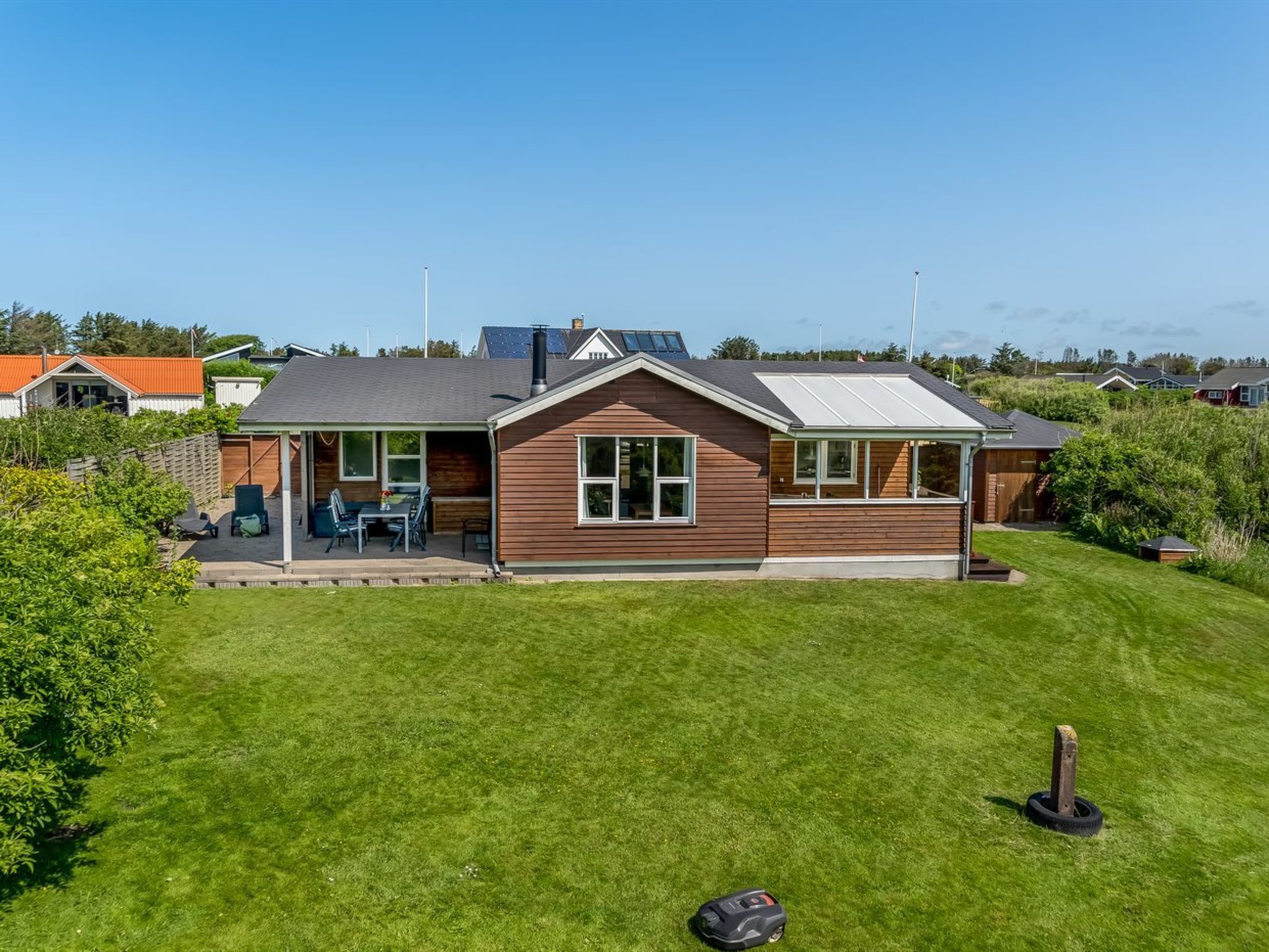 Une maison moderne dotée d’un patio couvert, d’une pelouse et d’un petit jardin.