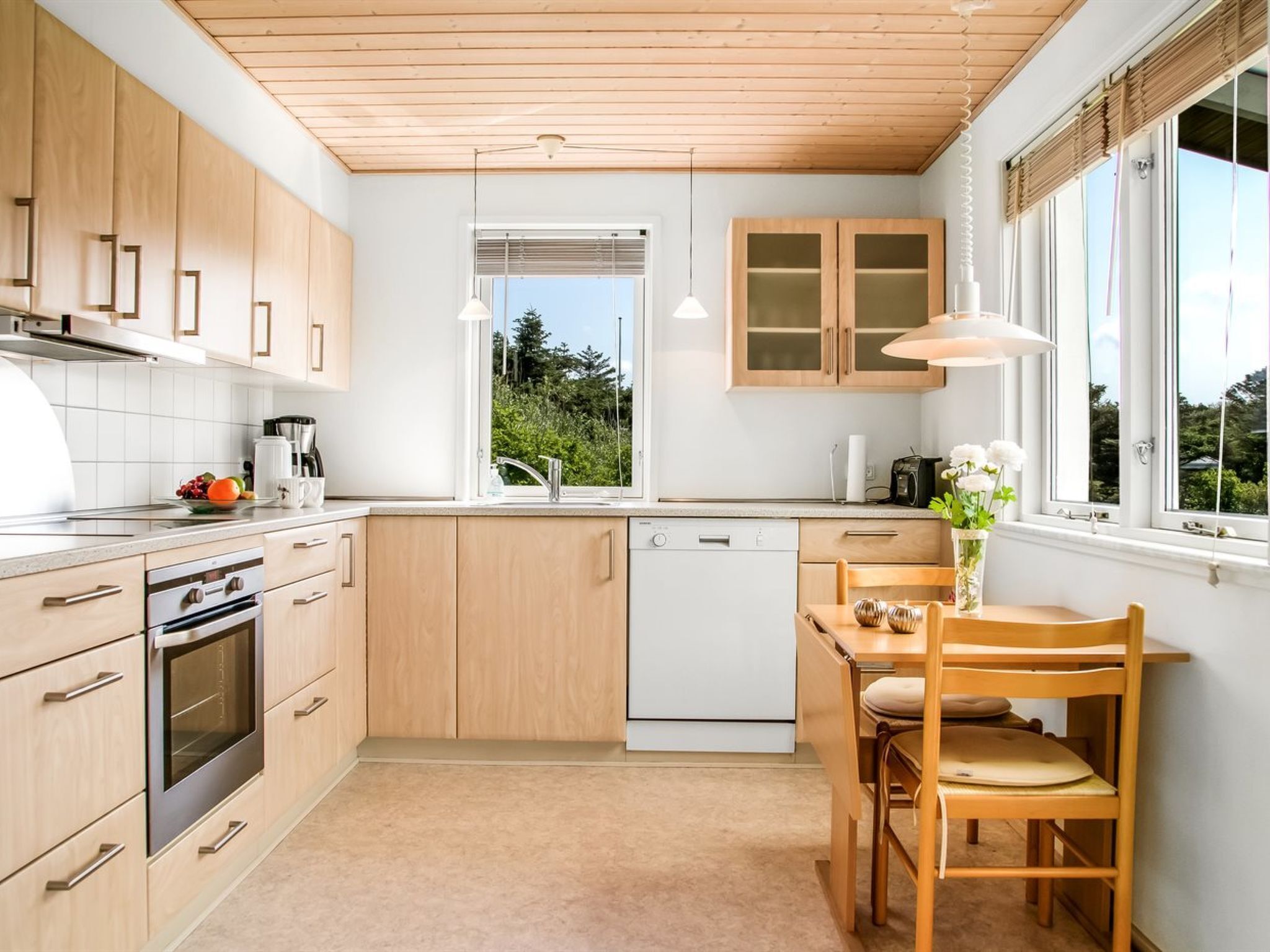 A modern kitchen with wooden cabinets, a built-in oven, a dishwasher, and a dining area with a table and chairs.