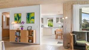 Un salon moderne avec un plancher en bois, un canapé en cuir noir, une table basse en bois et une bibliothèque remplie de livres et ornée d’un vase de fleurs.