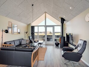 Un salon moderne avec un canapé en cuir noir, une table basse en bois, un fauteuil noir et une grande fenêtre donnant sur l’extérieur.