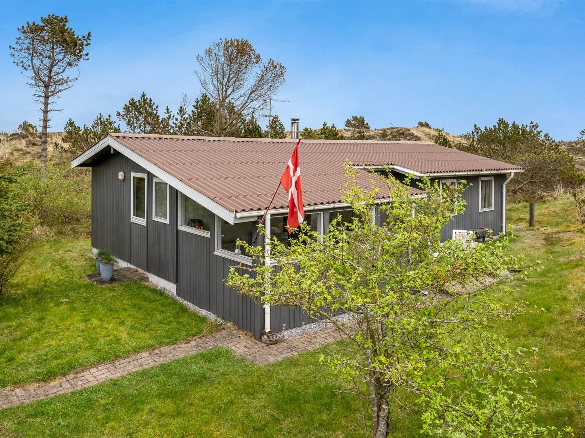 Ein zweistöckiges Haus mit geneigtem Dach, einer Fahnenstange mit einer Flagge und einem kleinen Garten.
