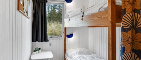 Een kleine kamer met een stapelbed, een bureau met een stoel, een raam met gordijnen en uitzicht op de omgeving.
