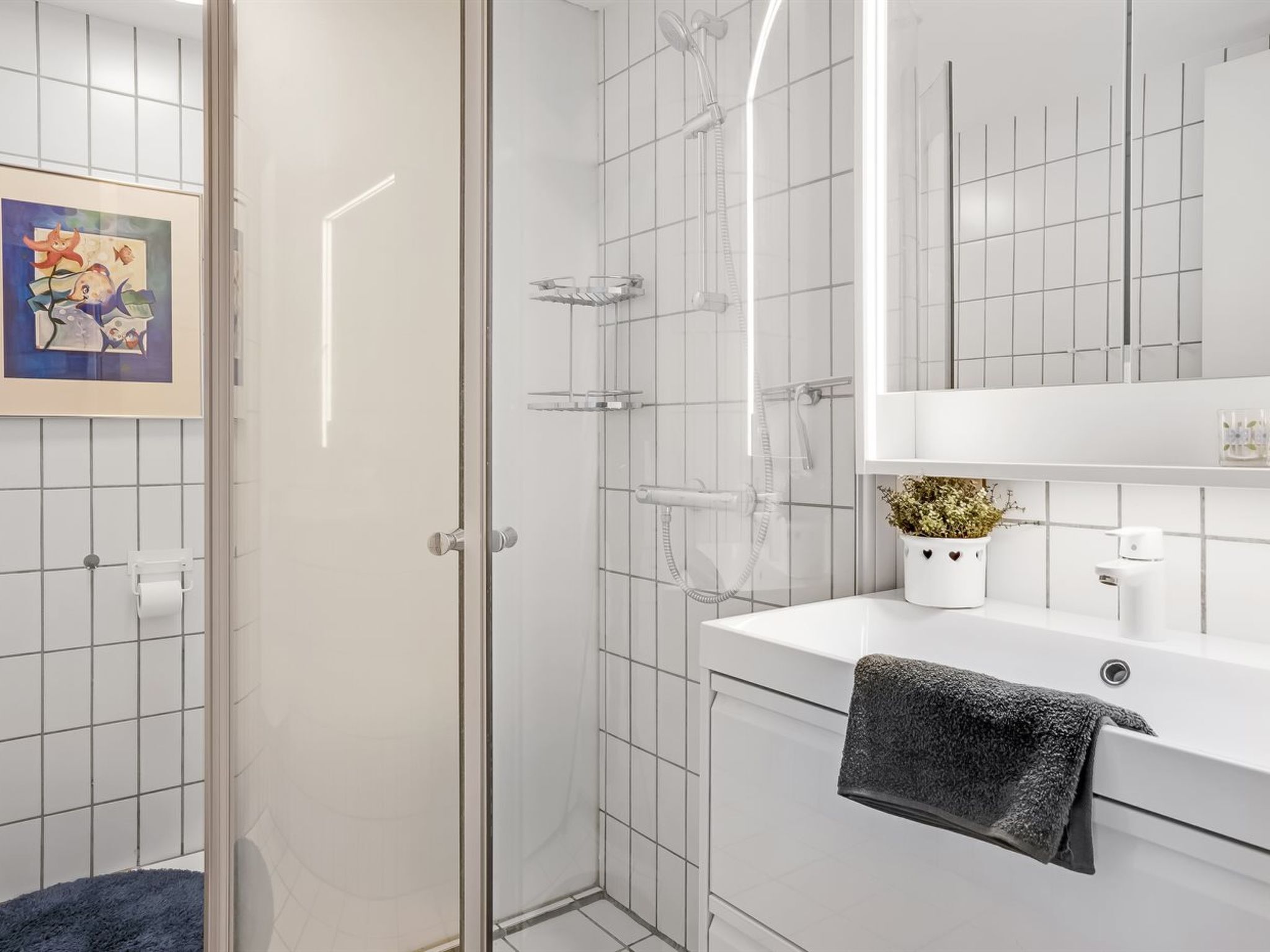 A modern bathroom with a glass shower enclosure, a white sink with a towel, and a framed picture on the wall.