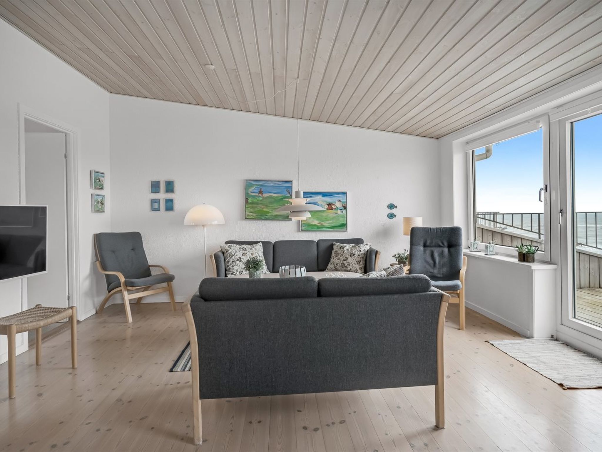Ein modernes Wohnzimmer mit einem grauen Sofa, zwei Sesseln, einem Fernseher und Kunstwerken an den Wänden.