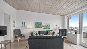 Un salon moderne avec un canapé gris, deux fauteuils, un téléviseur et des œuvres d’art accrochées aux murs.