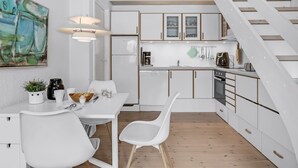 Une cuisine moderne avec des meubles blancs, un coin repas avec une table et des chaises blanches, et un escalier en bois.
