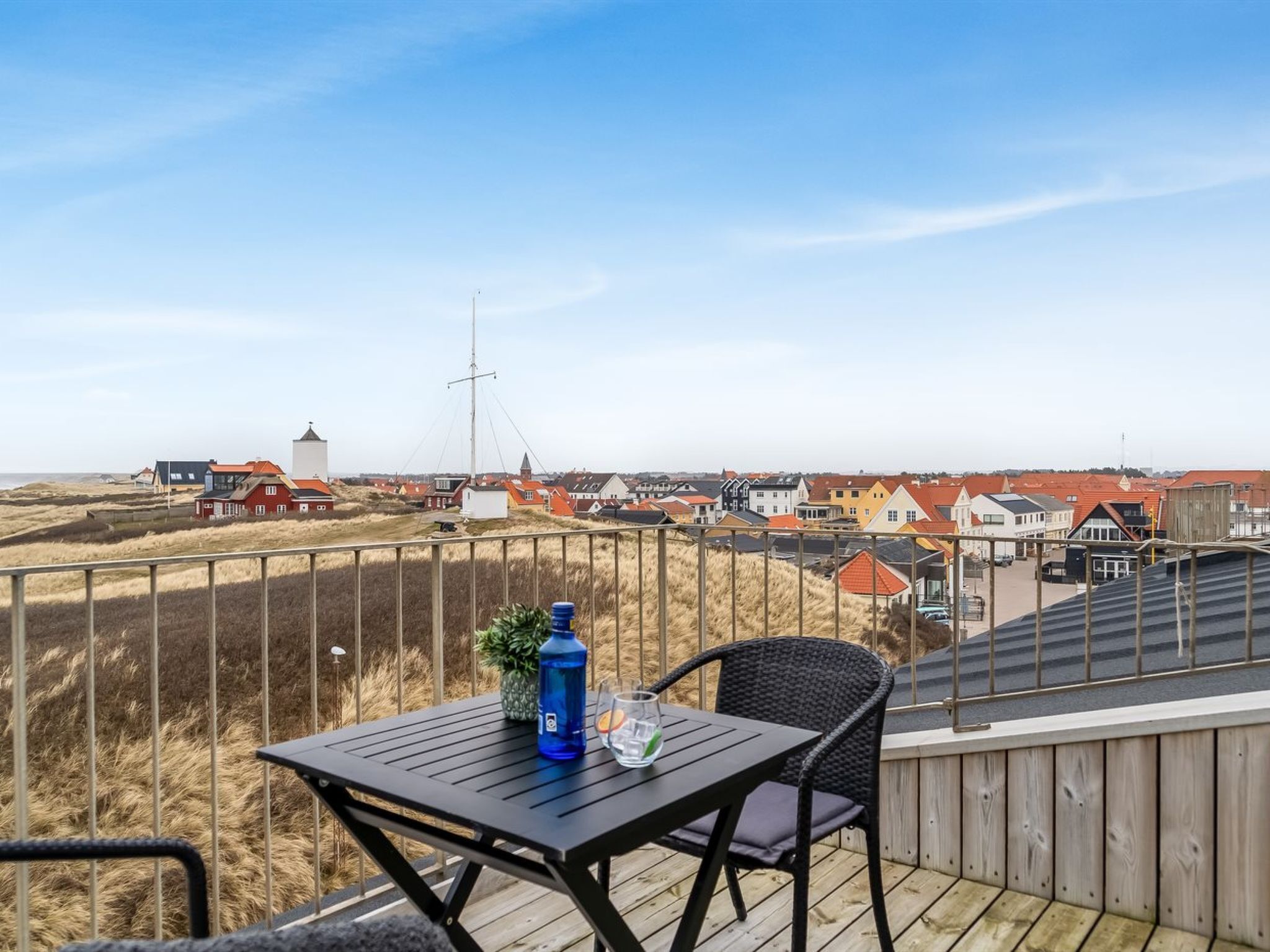 Eine Terrasse mit Tisch und Stuhl, mit Blick auf eine Küstenstadt mit Häusern und einem Leuchtturm.