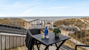 Un balcon avec une table, des chaises et une vue sur la plage et les dunes.