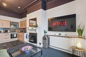 Un salon moderne doté d’une cheminée, d’un coin cuisine et d’un téléviseur fixé au mur qui affiche « NETFLIX ».