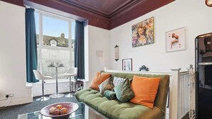 Una sala de estar con un sofá verde, una mesa de centro de cristal y vistas a un balcón.