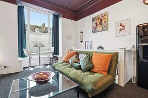 A living room with a green sofa, a glass coffee table, and a view of a balcony.