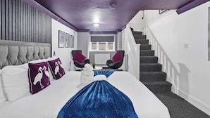 Una habitación de hotel con una cama, dos sillas, una escalera y un ventanal.