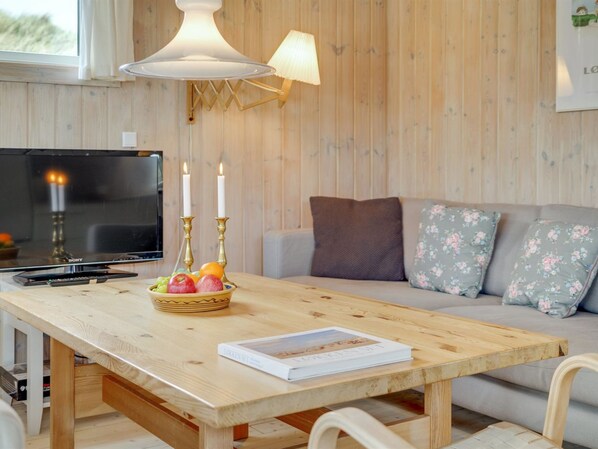 A cozy living room with a wooden table, a sofa, a TV, and a bowl of fruit.
