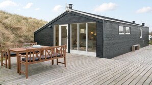 A modern cabin with a wooden deck, large sliding glass doors, and a small outdoor seating area.