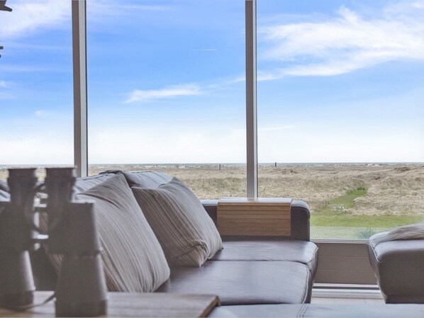 A modern living room with a large window offering a view of a beach and dunes.