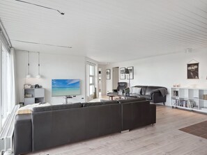 A modern living room with a large black sectional sofa, a flat-screen TV, and a dining area with a table and chairs.