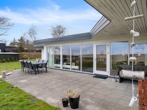Une maison moderne dotée d’un patio, d’un espace salon extérieur et d’une pièce entièrement vitrée.