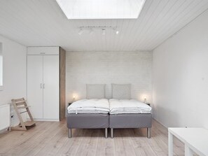 A bedroom with a skylight, a bed with two pillows, a bedside table, and a radiator.