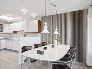 Une cuisine moderne avec des meubles blancs, une table à manger avec des chaises et des luminaires suspendus.