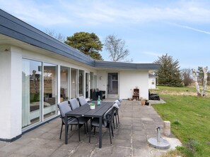 Une maison moderne dotée d’un patio, d’une table à manger avec des chaises et d’une grande porte-fenêtre coulissante.