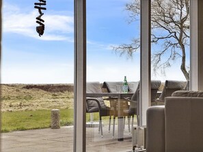 Ein Zimmer mit einem großen Fenster und Blick auf ein grasbewachsenes Feld und einen Baum.