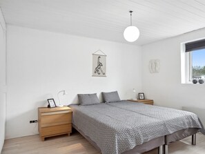Une chambre à coucher au style minimaliste, avec un lit, des tables de chevet, une lampe suspendue et une fenêtre.