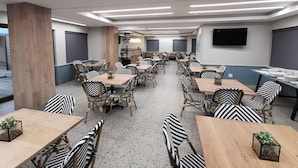 A modern dining area with wooden tables and black-and-white patterned chairs, a flat-screen TV on the wall, and a large pillar. - All Africa House (Cape Town)