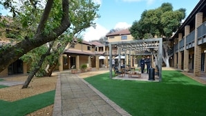 A courtyard with a covered seating area, brick buildings, and green artificial grass. - All Africa House (Cape Town)